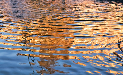 ripples on the surface of the water with the reflection of the sunset from buildings and trees
