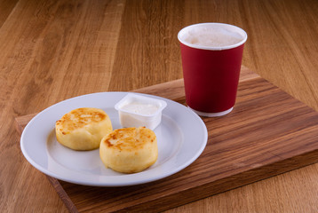 Cheesecakes, are served in a plate with sour cream and a cup of coffee