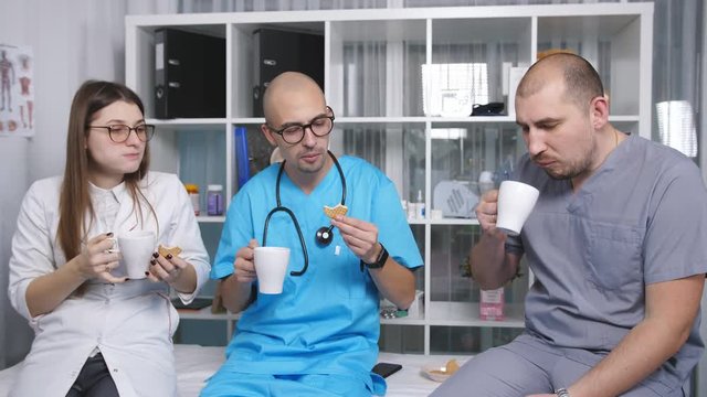 Three doctors in the staffroom talk and drink coffee at the break.