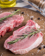 Fresh pork meat on a wooden board with rosemary, salt and pepper. Closeup