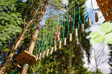 Little girl on a ropes course in a treetop adventure park passing hanging rope obstacle