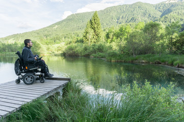 Disabled man on wheelchair enjoying and looking at beautiful nature on lake pier