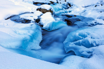 Mountain river in winter time in a frozen blue ice and pure snow