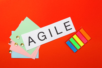 Word AGILE and stationery on color background