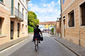 old woman in bike going to traditional market to do grocery in small old italian town