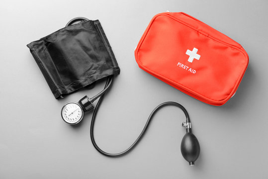 Sphygmomanometer and first aid kit on grey background. Health care concept