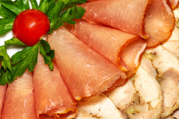 slicing different meats in a plate with tomato and green leaves on plate
