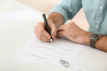 Young man signing decree of divorce at table, closeup