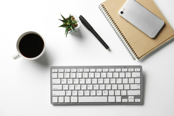 Computer keyboard, notebook, phone, cup of coffee and succulent on white table