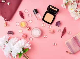 Flat lay woman accessories with cosmetic, facial cream, bag, flowers on bright pink table.
