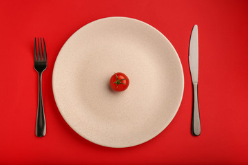 Plate with one tomato and cutlery on color background. Diet concept