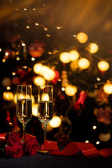 Glasses of champagne on the background of lights with roses and red ribbon