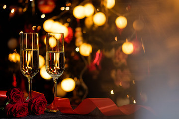 Glasses of champagne on the background of lights with roses and red ribbon