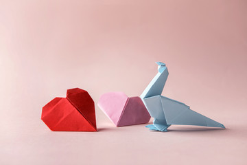 Origami bird and hearts on color background