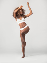Happy beautiful African American Girl with wild curly hair and wearing underwear in studio with a gray background 