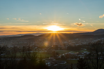 Fototapeta premium Sonnenuntergang mit Stadt im Vordergrund und Bergen im Hintergrund