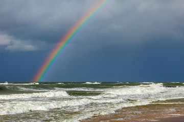 Bright rainbow on the background of storm clouds over the raging sea