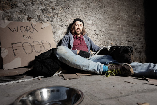 Man in dirty rags hugging dog sitting on sidewalk