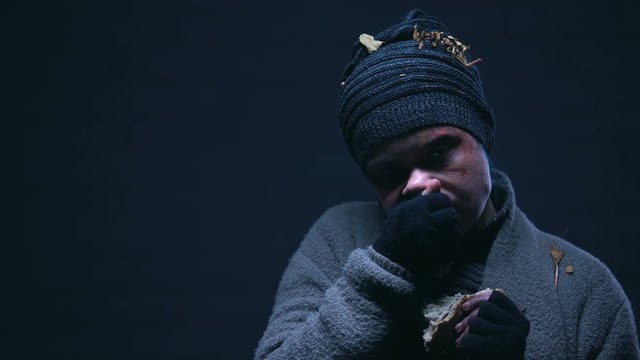 Distrustful homeless person starving from hunger eating piece of bread, charity