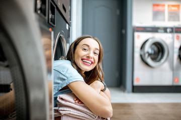Portrait of a cheerful woman with clean and fresh towels sitting on the dryer machine in the laundry