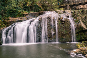 Fototapeta na wymiar A running waterfall of river through the rocks of the mountain in autumn.
