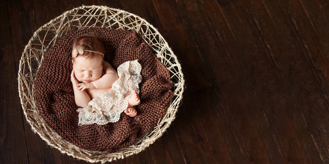 Fototapeta na wymiar Sweet newborn baby girl sleeps in the basket. Dark brown background. Copy space