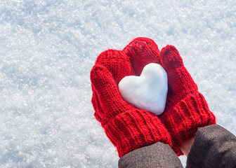 Female hands in knitted mittens with heart of snow in winter day. Love concept. Valentine day background. - obrazy, fototapety, plakaty