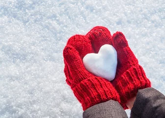 Foto auf Leinwand Female hands in knitted mittens with heart of snow in winter day. Love concept. Valentine day background. © augusta16