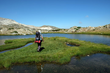 Fototapeta premium A hiker is walking on grassy island in glacial lake