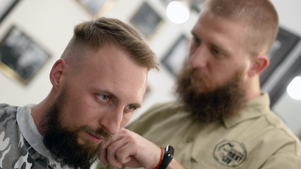 The barber is cutting the client's hair with electric razor. He wears black rubber glove on hand