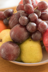 Close-up: fresh fruits on a plate are on a wooden table. Vertical image. Concept: healthy food and tasty diet.