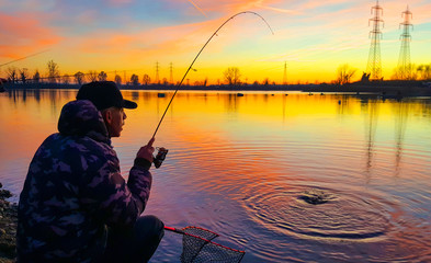 fisherman who caught a fish in a pond at sunset