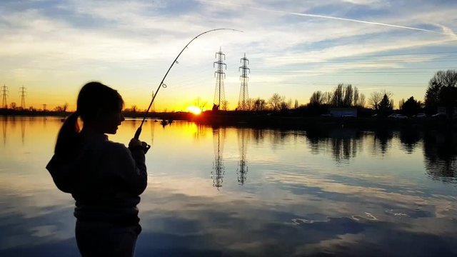 young girl fishing in a pond at sunset