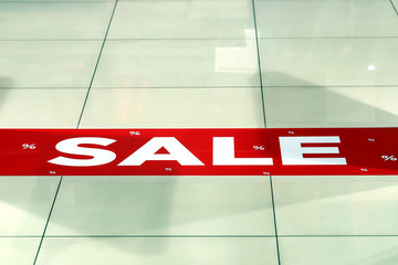 Red and white inscription Sale on the background of  a tiled floor  in the store. Mall Discount...