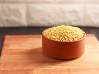 Raw bulgur in a clay bowl on a wooden board