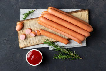 Raw frankfurter sausages with ketchup on cutting board. Top view. - obrazy, fototapety, plakaty