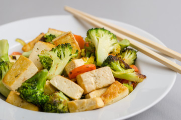 Grilled tofu with broccoli and carrots in white plate with chopsticks on the right side.
