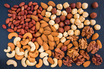 Assortment of nuts on a black slate background top view. Concept healthy snack.