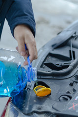 Pouring antifreeze liquid for washing car screen.