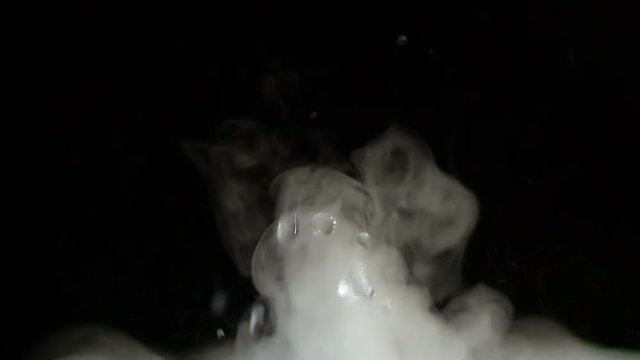 Splashes and Fog on a Black Background. A mixture of liquid and white smoke intensively boils at the bottom of the screen on a black background