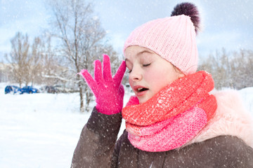 girl in a coat and a knitted cap with a bubo shakes off the snow