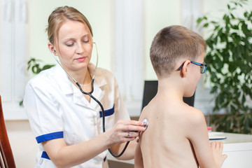 Kobieta lekarz pulmonolog podczas badania. Osłuchuje płuca chłopca stetoskopem w gabinecie lekarskim.    - obrazy, fototapety, plakaty