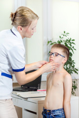 Chłopiec w okularach badania lekarskiego. Lekarka w gabinecie lekarskim podczas badania migdałków u chłopca w okularach - obrazy, fototapety, plakaty