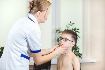 Lekarka w gabinecie lekarskim podczas badania migdałków u chłopca w okularach - obrazy, fototapety, plakaty