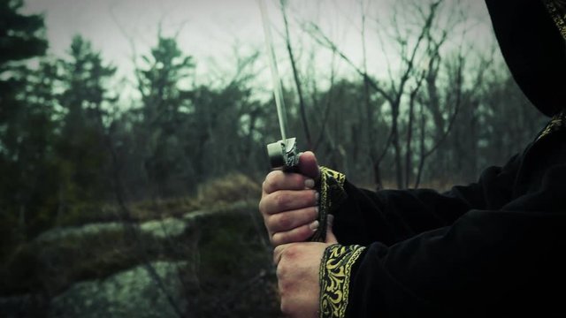 Sword being pulled from its sheath by hooded figure in a robe.