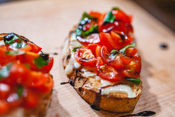 Traditional Italian bruschetta with cherry tomatoes, cheese, basil and balsamic vinegar on wooden board. Close up - obrazy, fototapety, plakaty