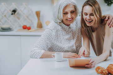 Mature and young women are laughing while watching photos indoor