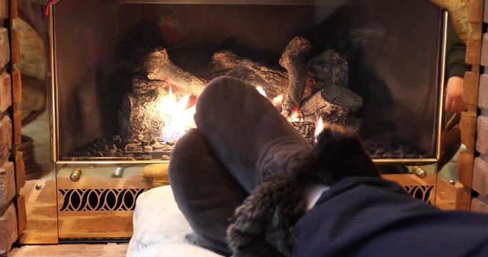 Fuzzy slippers on fireplace hearth with burning logs on winter day.