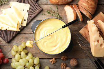 Flat lay composition with pot of delicious cheese fondue on wooden table