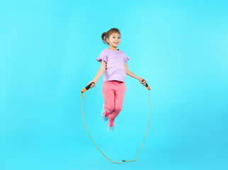 Full length portrait of girl jumping rope on color background